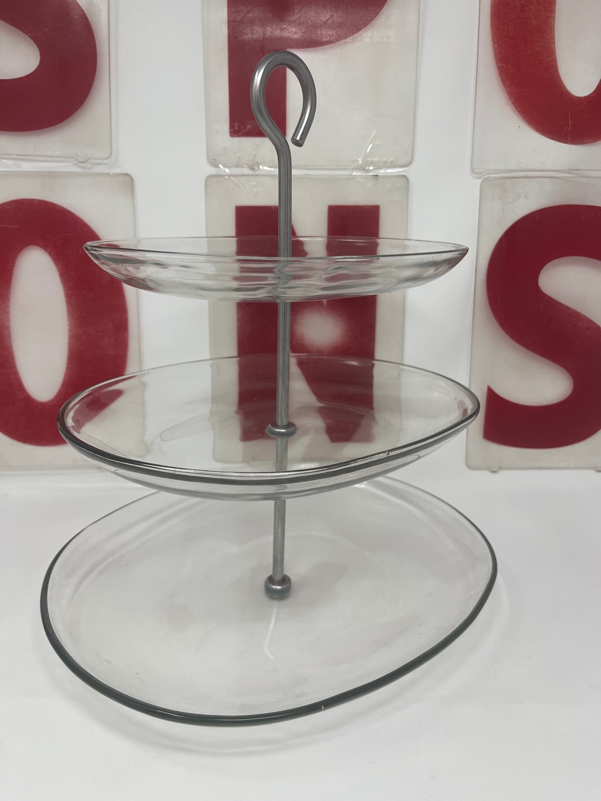 Three-tier oval glass serving stand with stainless steel base, featuring three glass trays and a sturdy central pole for displaying appetizers and desserts.