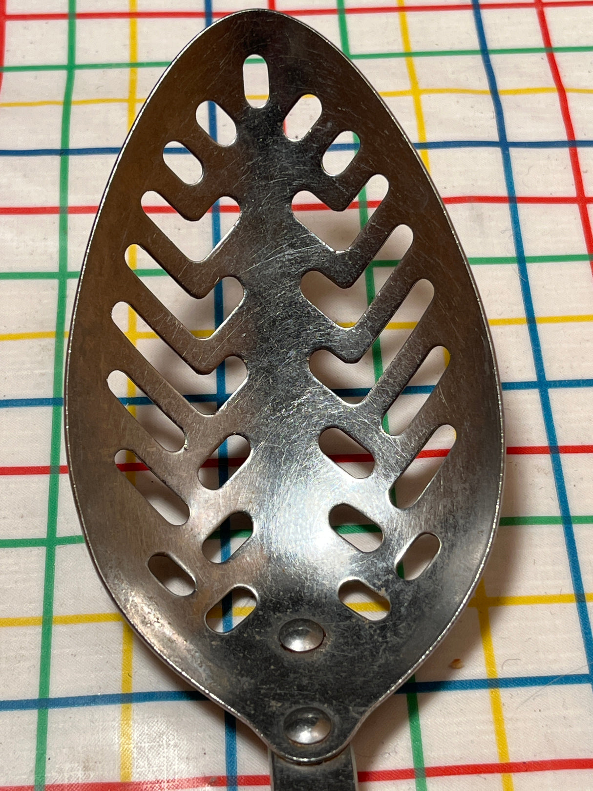 Slotted serving spoon with a perforated stainless steel bowl and black Bakelite handle, designed by EKCO Forge for efficient liquid drainage during serving.