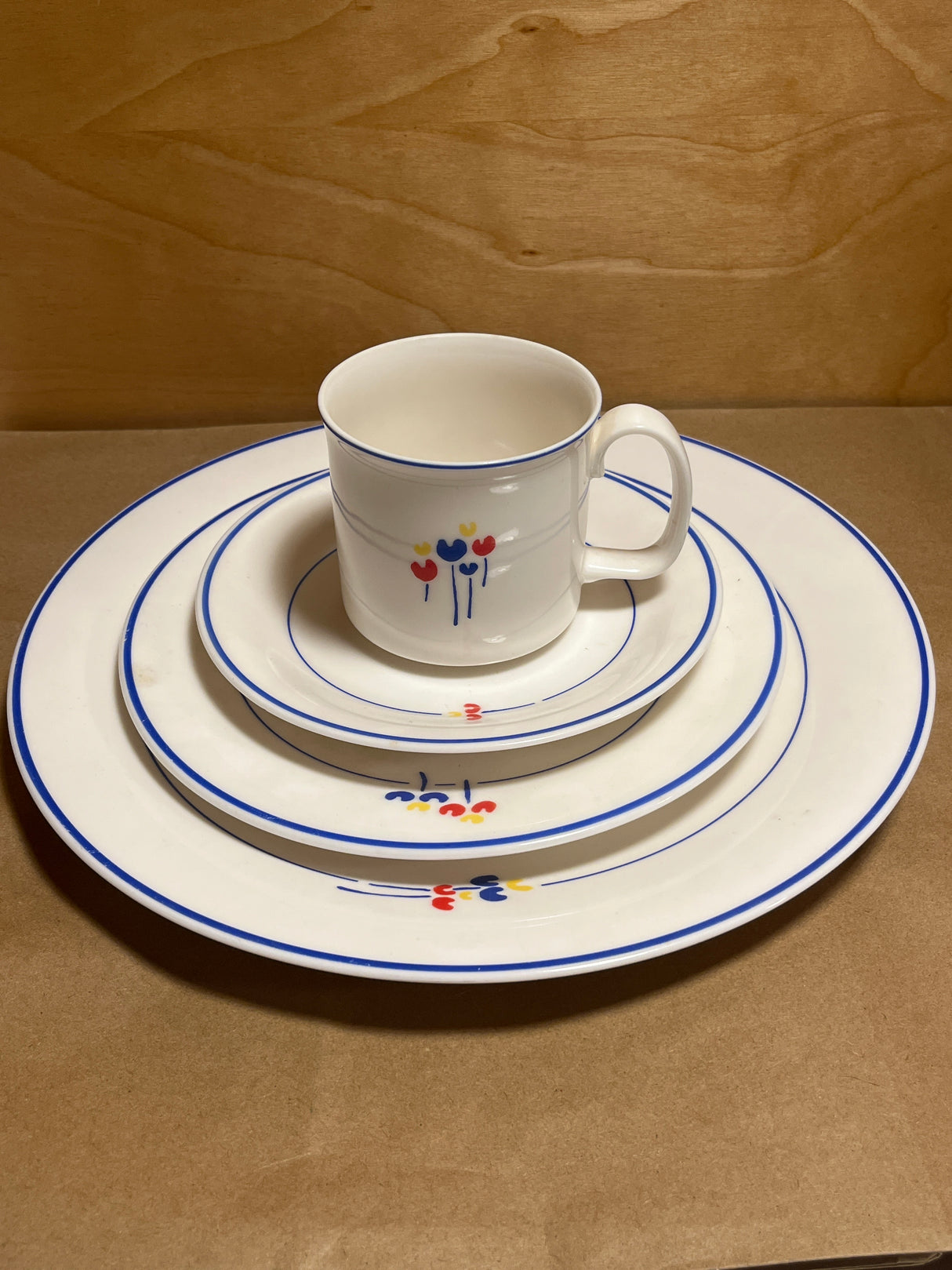 Rival Designs Tulip dinnerware collection Lot 3078: A stacked set of white ceramic plates and a mug, featuring blue rims and colorful floral motifs.