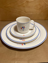Rival Designs Tulip dinnerware collection Lot 3078: A stacked set of white ceramic plates and a mug, featuring blue rims and colorful floral motifs.