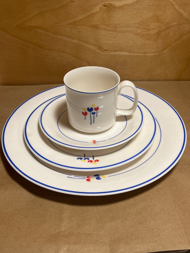 Rival Designs Tulip dinnerware collection Lot 3078: A stacked set of white ceramic plates and a mug, featuring blue rims and colorful floral motifs.
