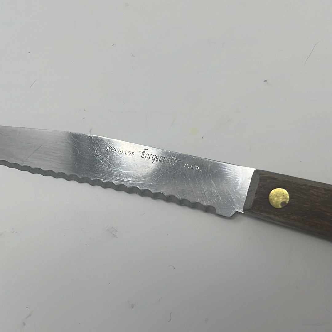 A serrated Forgecraft knife with a wooden handle, ideal for slicing tomatoes in summer.