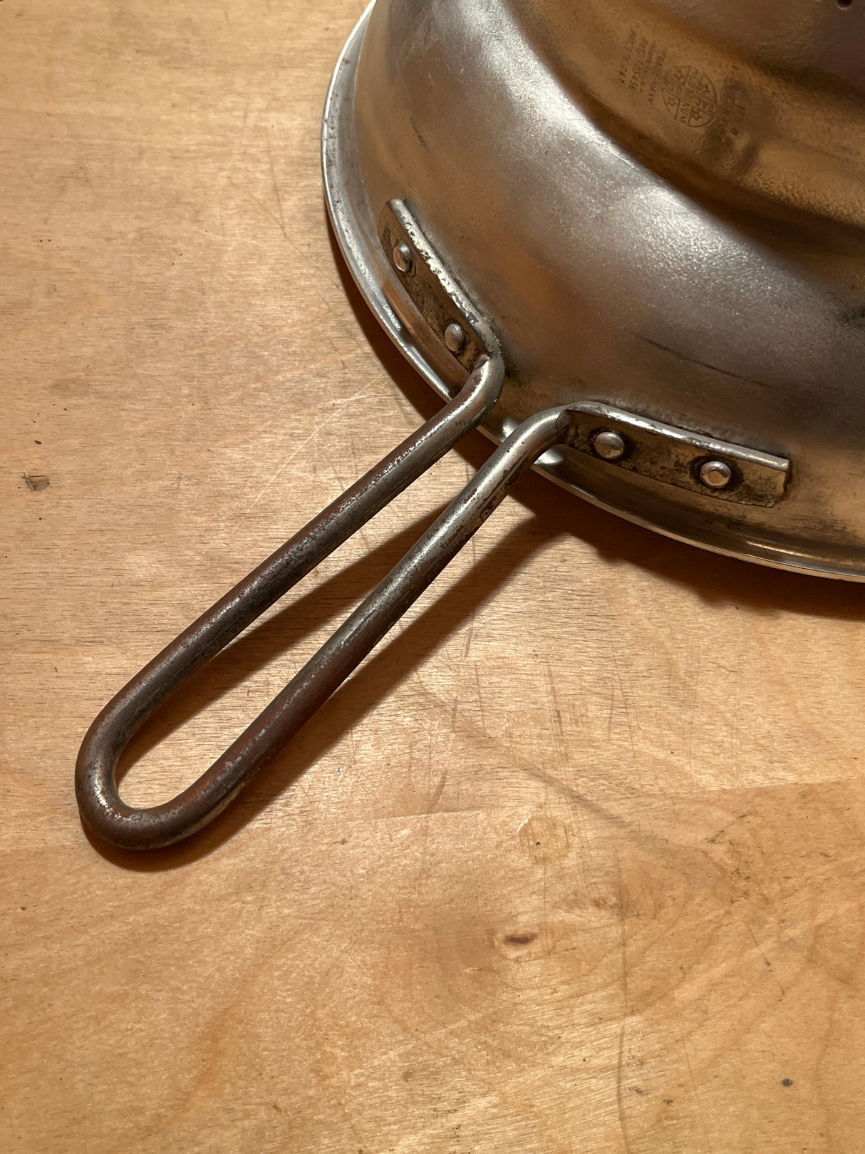 Tiny pointy cone sieve strainer - aluminum, shown upside-down with a riveted handle on a wooden surface, highlighting its sturdy construction and minor dent at the tip.
