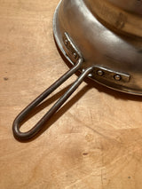 Tiny pointy cone sieve strainer - aluminum, shown upside-down with a riveted handle on a wooden surface, highlighting its sturdy construction and minor dent at the tip.