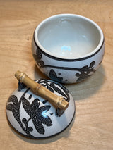 Set of 8 white mugs and sugar bowl with lid featuring a black dotted floral-vine pattern and bamboo handle on a light wood surface.