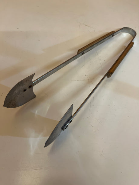 Vintage grill tongs with wood handles, featuring metal jaws shaped like paddle blades, ideal for handling coals or food on a grill.