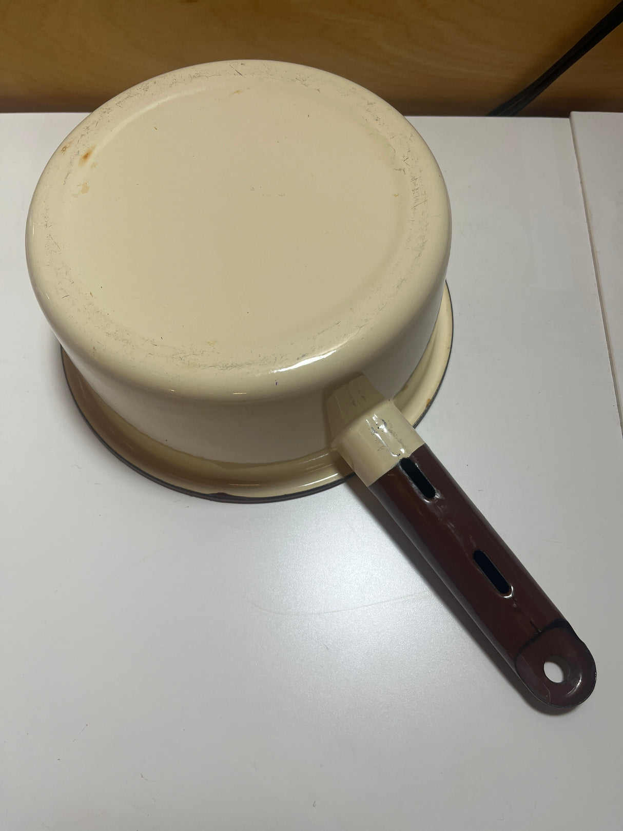 Close-up of a tan and brown enameled sauce pot, featuring a chip on the handle's end with a hanging notch.