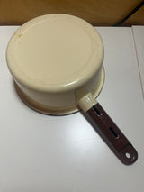 Close-up of a tan and brown enameled sauce pot, featuring a chip on the handle's end with a hanging notch.