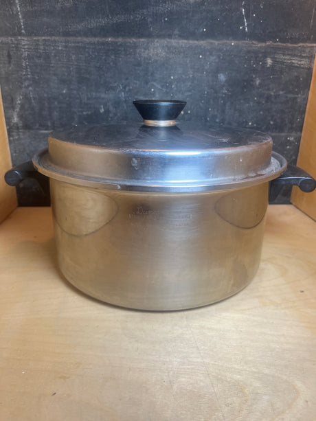 Stock pot with lid and black handles - vintage Duncan Hines 3-ply 18-8 stainless steel, featuring plastic handles and knob, on a wooden surface.