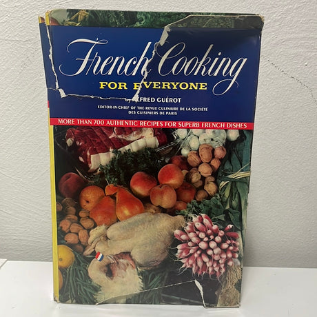 French Cooking for Everyone cookbook on a table, featuring images of food, fruits, and radishes, highlighting authentic French recipes and culinary inspiration.