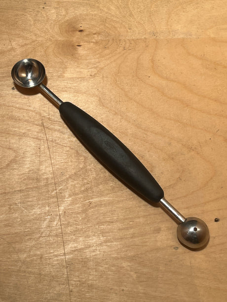 Melon baller with silicone handle - OXO Good Grips, featuring a double-ended design with metal scoops for carving fruit or portioning ingredients, on a wooden surface.