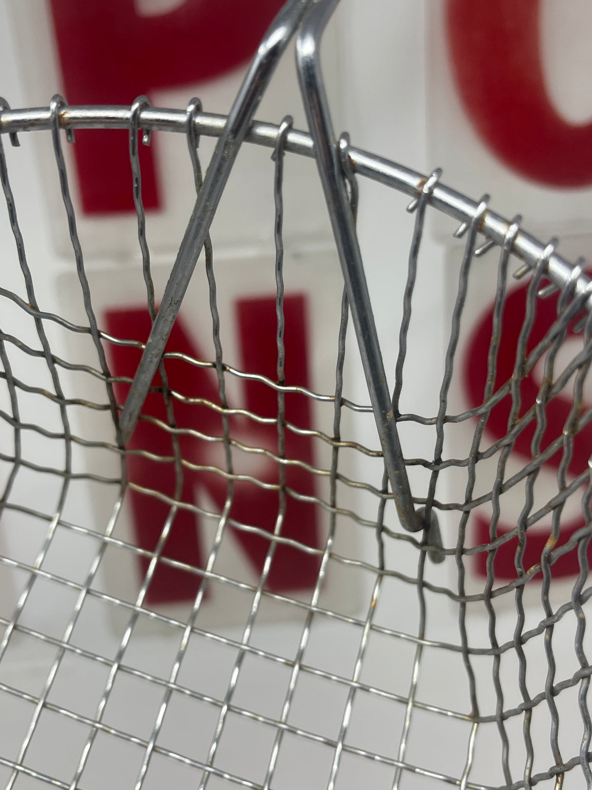 Close-up of an alloyed steel deep-fryer basket with a white resin handle, highlighting its wire mesh construction and removable handle feature for easy cleaning.