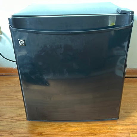 GE Spacemaker Compact Refrigerator with Freezer on wood floor, includes removable wire rack, small dent on corner; ice cube test passed successfully.