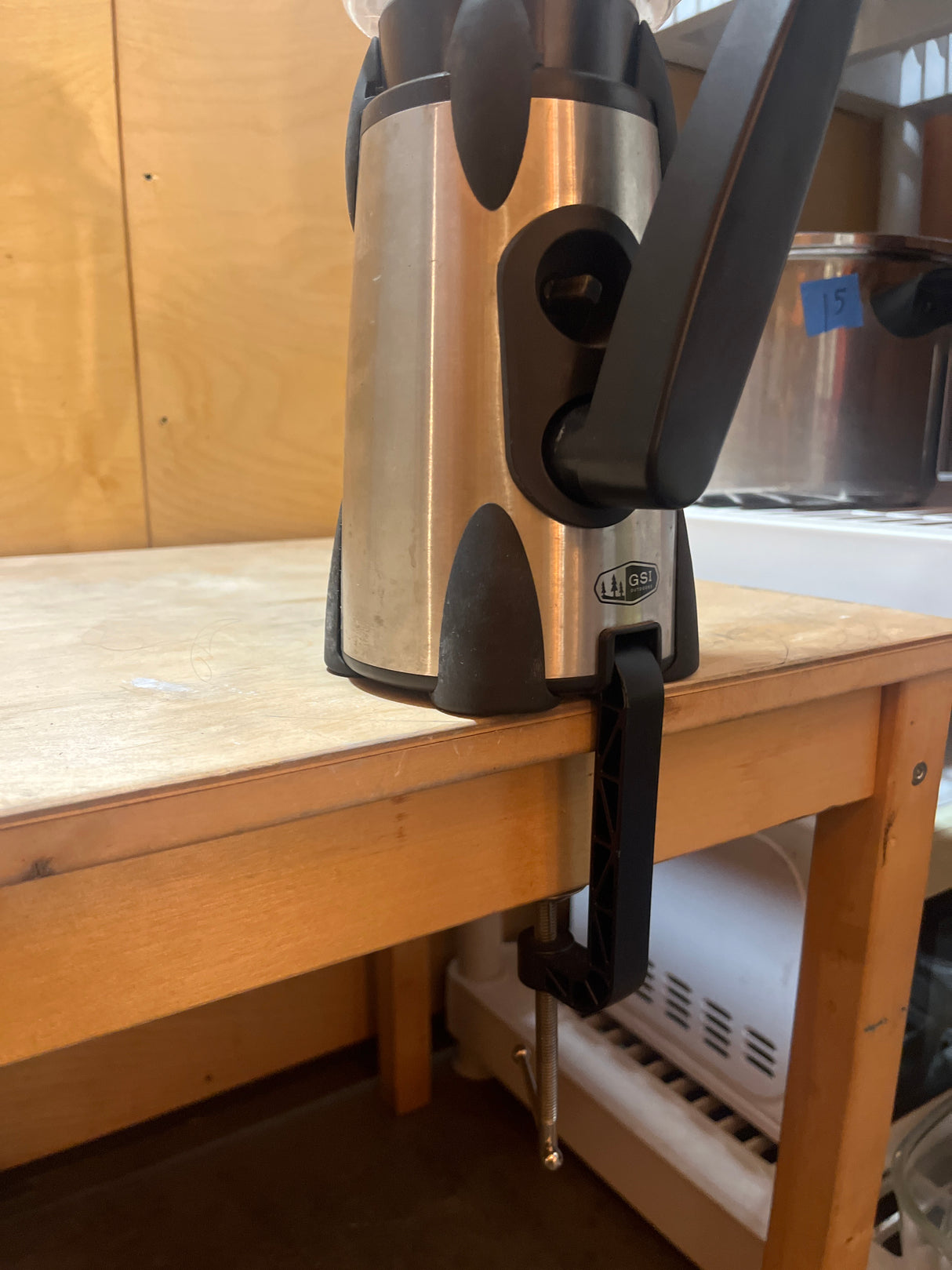 GSI Outdoors Vortex hand-cranked blender clamped on table edge, showcasing its sturdy stainless-steel body, long handle, and securing mechanism for outdoor blending.