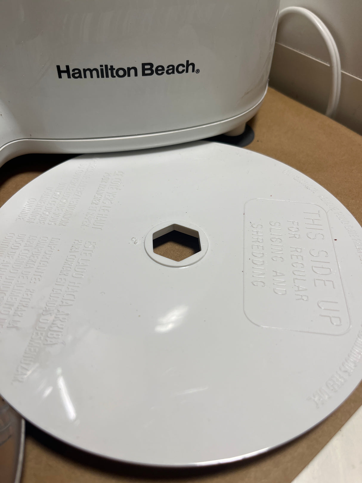 Hamilton Beach Chef Prep 70700 7-cup food processor with slicing/shredding disc, showing hex-shaped center hole and instructions; small chip on rim visible.