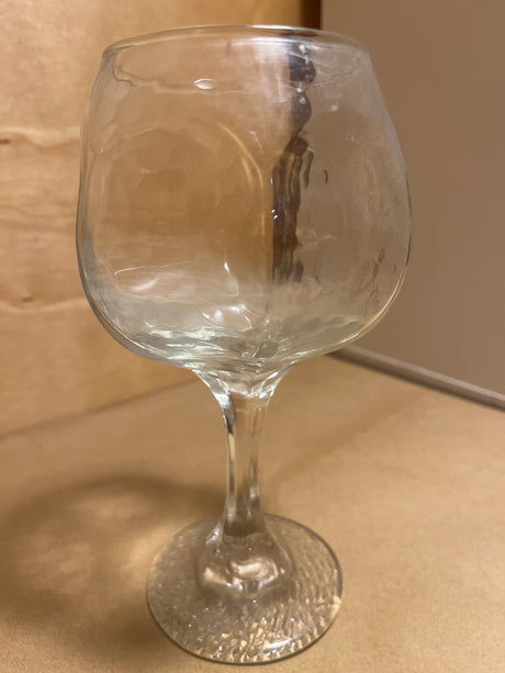 Libbey Chivalry glassware featuring a clear, dimpled goblet-style glass with a rounded bowl, slender stem, and textured circular base on a tan surface.