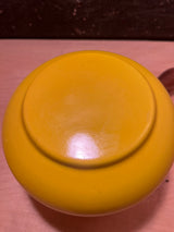 Vintage enamel sunshine yellow fondue pot with visible foot ring, flipped upside-down on wooden surface; glossy finish shows surface scratches, complemented by wood handles.