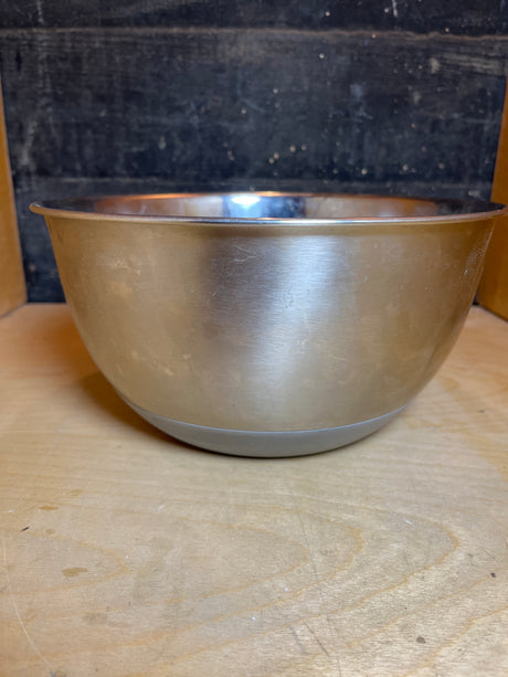 Stainless steel mixing bowl with gray silicone nonskid base on wooden surface, featuring high sides for stability during baking projects.