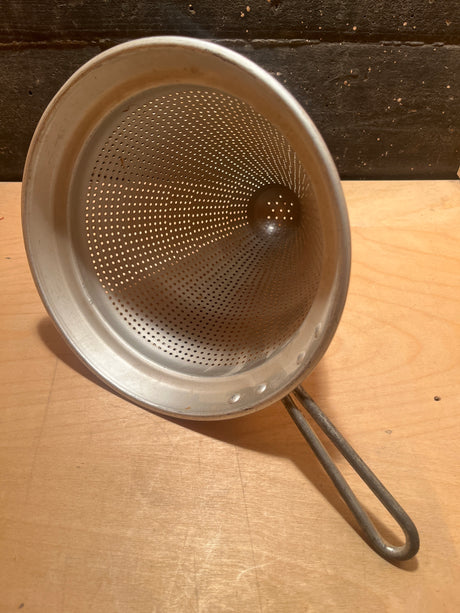 Cone strainer with fine perforations and a long looped handle, ideal for filtering liquids like stocks and sauces to remove solids.