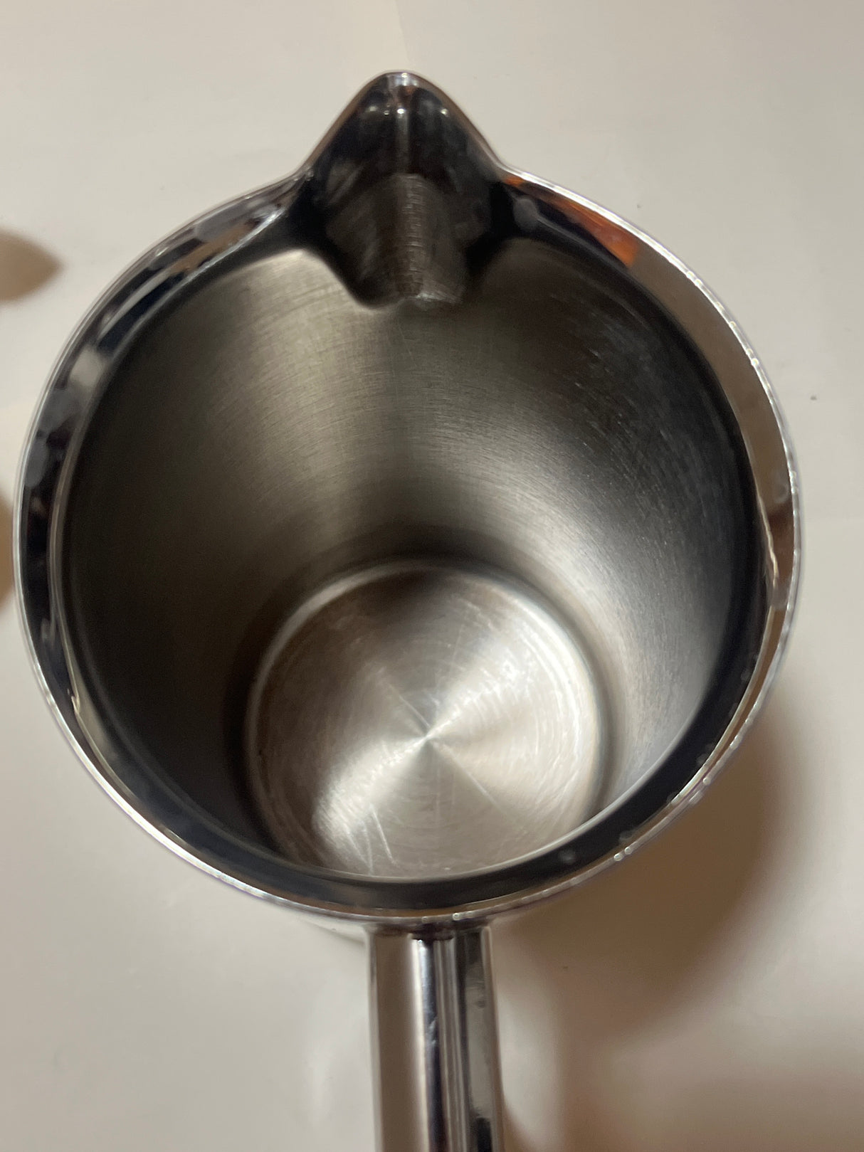 Looking down into a Frieling stainless steel French press coffee maker, showcasing its sleek interior, small spout, and visible handle at the base.