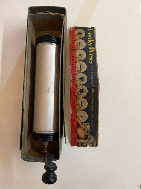 Vintage Cooky Press in original box with aluminum cylinder, crank handle, black end caps, and interchangeable discs for shaping decorative cookies efficiently.