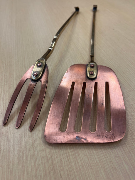 Set of copper grill tools with brass handles, featuring a spatula and grill tong, designed for durability and heat protection, with minor tarnish visible.