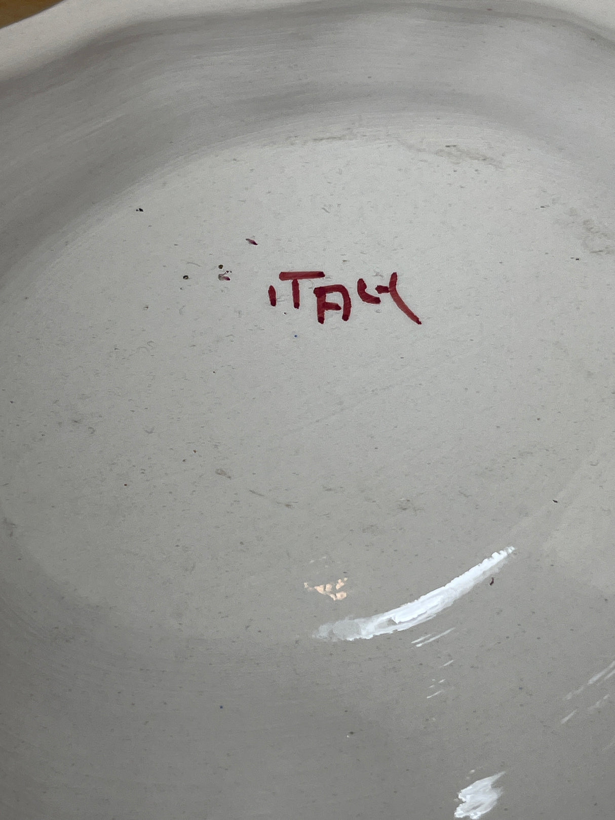 Underside of a plain off-white ceramic plate with ITALY in red, hand-painted. Part of porcelain soup tureen set with red roses.