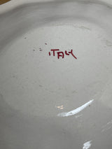 Underside of a plain off-white ceramic plate with ITALY in red, hand-painted. Part of porcelain soup tureen set with red roses.