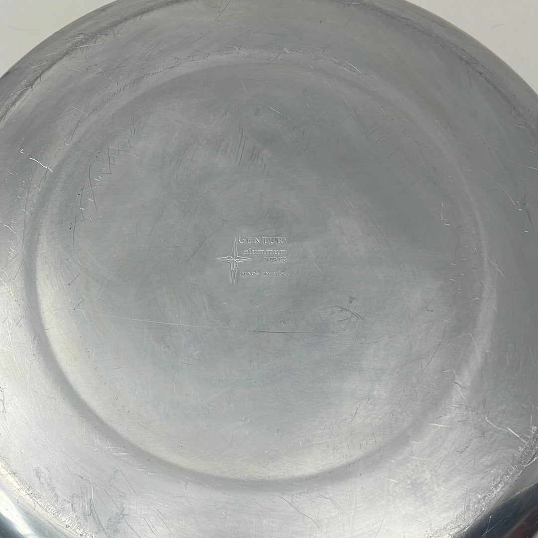 A close-up of Century Ware stock pot with steamer basket, featuring a silver pan and metal bowl on a grey surface, with logo details visible.