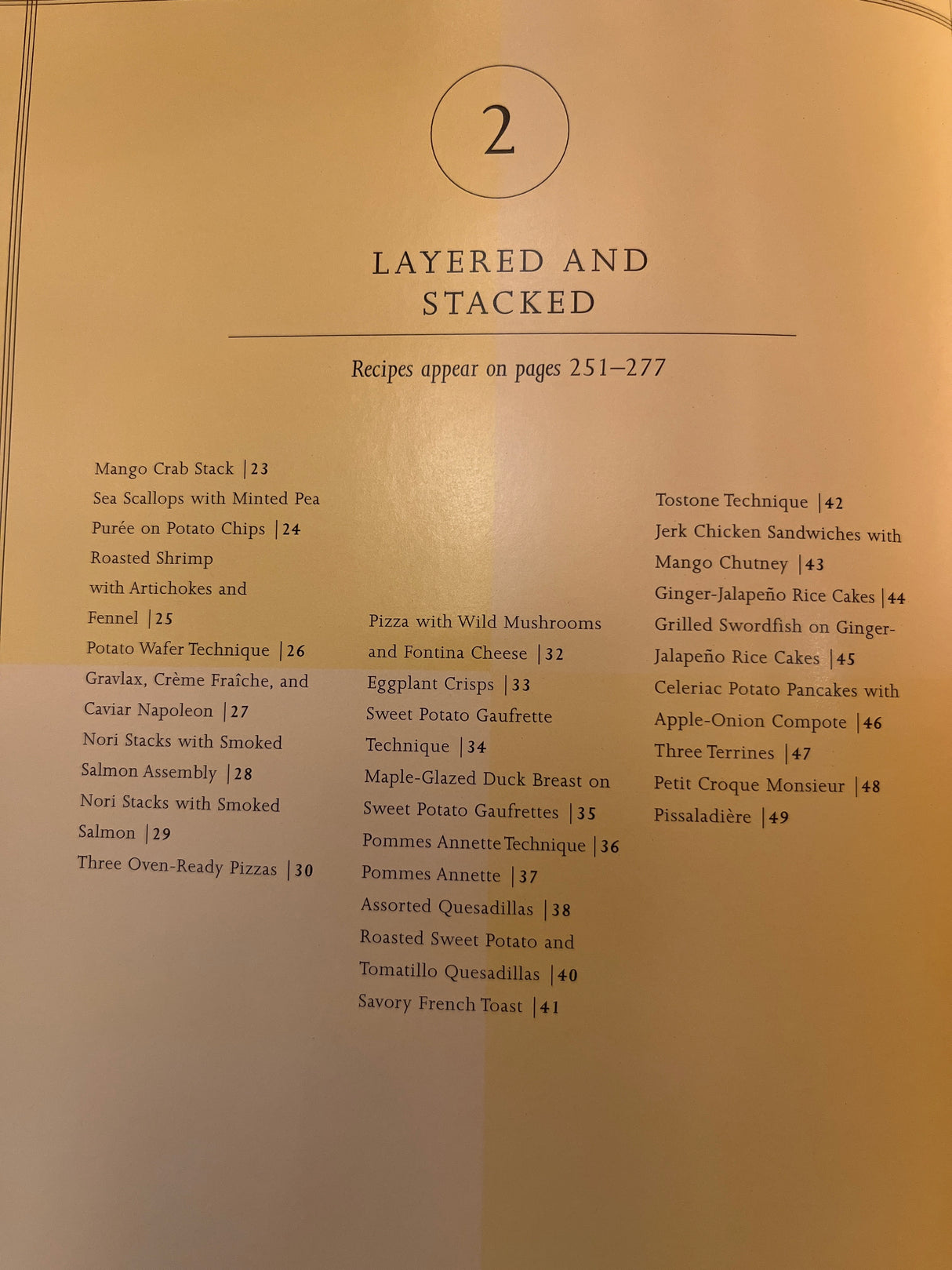 Martha Stewart’s Agora D’oeuvres cookbook section opener, showcasing LAYERED AND STACKED recipes, lists dishes like Mango Crab Stack and Pissaladière with page numbers.