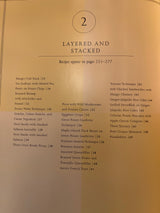 Martha Stewart’s Agora D’oeuvres cookbook section opener, showcasing LAYERED AND STACKED recipes, lists dishes like Mango Crab Stack and Pissaladière with page numbers.