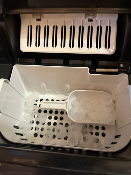 Portable countertop ice maker - Hamilton Beach: Ice-collection bin with plastic scoop on fresh bullet-style ice cubes, part of a compact, freestanding ice maker producing 26 lbs. daily.