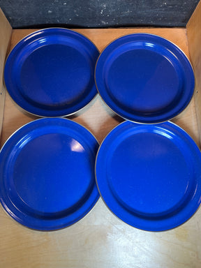 Set of 4 blue speckled enamelware plates with glossy finish, neatly stacked on a wooden shelf, showcasing their lightweight, durable design for versatile use.