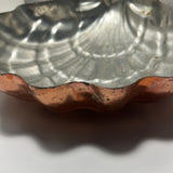 Close-up of a "Large copper seashell baking pan with nickel lining" by [Brand Name] with scalloped edges and a reflective surface casting a shadow.