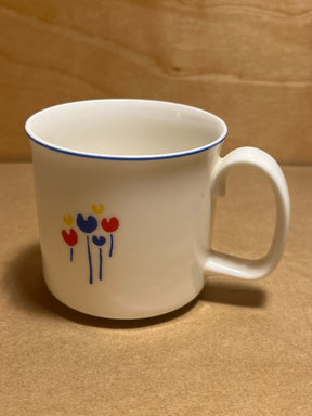 Rival Designs Tulip dinnerware collection Lot 3078 features a white ceramic mug with a blue-edged lip and minimalist floral motif, showcasing tulip-like blooms and blue stems.