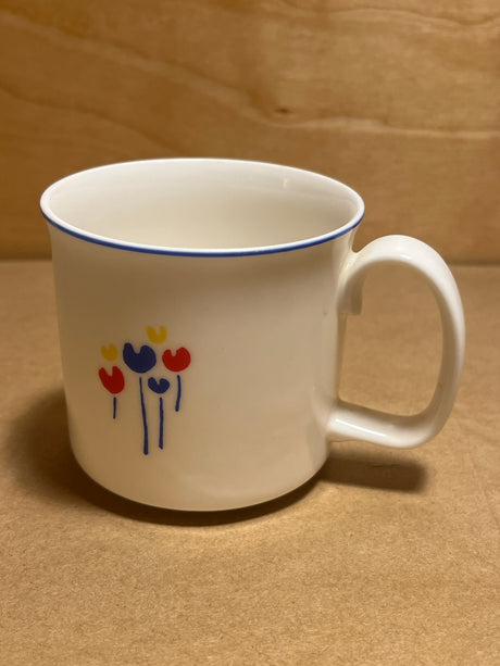 Rival Designs Tulip dinnerware collection Lot 3078 features a white ceramic mug with a blue-edged lip and minimalist floral motif, showcasing tulip-like blooms and blue stems.