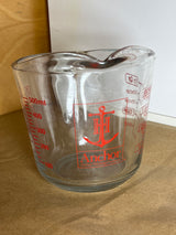 Anchor Hocking glass 2-cup measuring cup with handle, featuring red volume markings and logo, sits empty on a wooden surface.