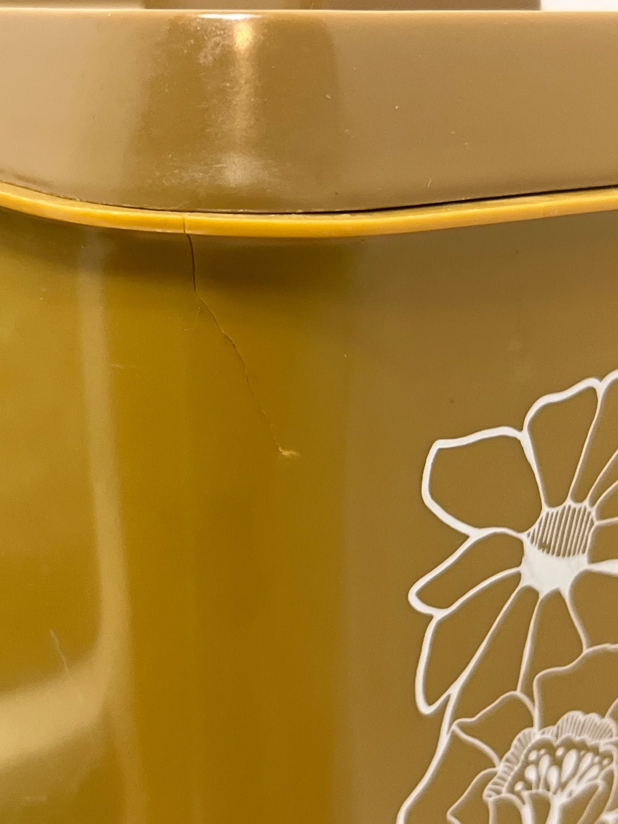 Close-up of a mustard Melmac container with a white floral decal and a crack near the lid, part of a retro storage set of four.
