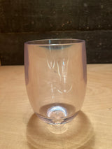 Stemless hard acrylic wine glass with gently curved sides and a smooth rim, featuring subtle iridescent highlights, sits on a light-wood tabletop.