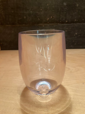 Stemless hard acrylic wine glass with gently curved sides and a smooth rim, featuring subtle iridescent highlights, sits on a light-wood tabletop.
