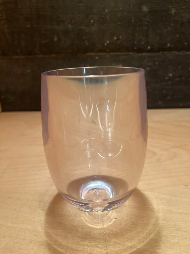 Stemless hard acrylic wine glass with gently curved sides and a smooth rim, featuring subtle iridescent highlights, sits on a light-wood tabletop.