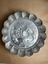 Copper baking pan with embossed fruit design; vintage-style fluted mold featuring pears, grapes, and pineapple, often used as decorative kitchen wall art.