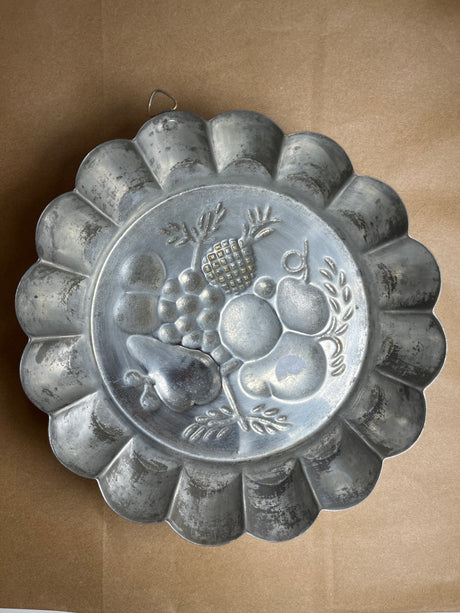 Copper baking pan with embossed fruit design; vintage-style fluted mold featuring pears, grapes, and pineapple, often used as decorative kitchen wall art.