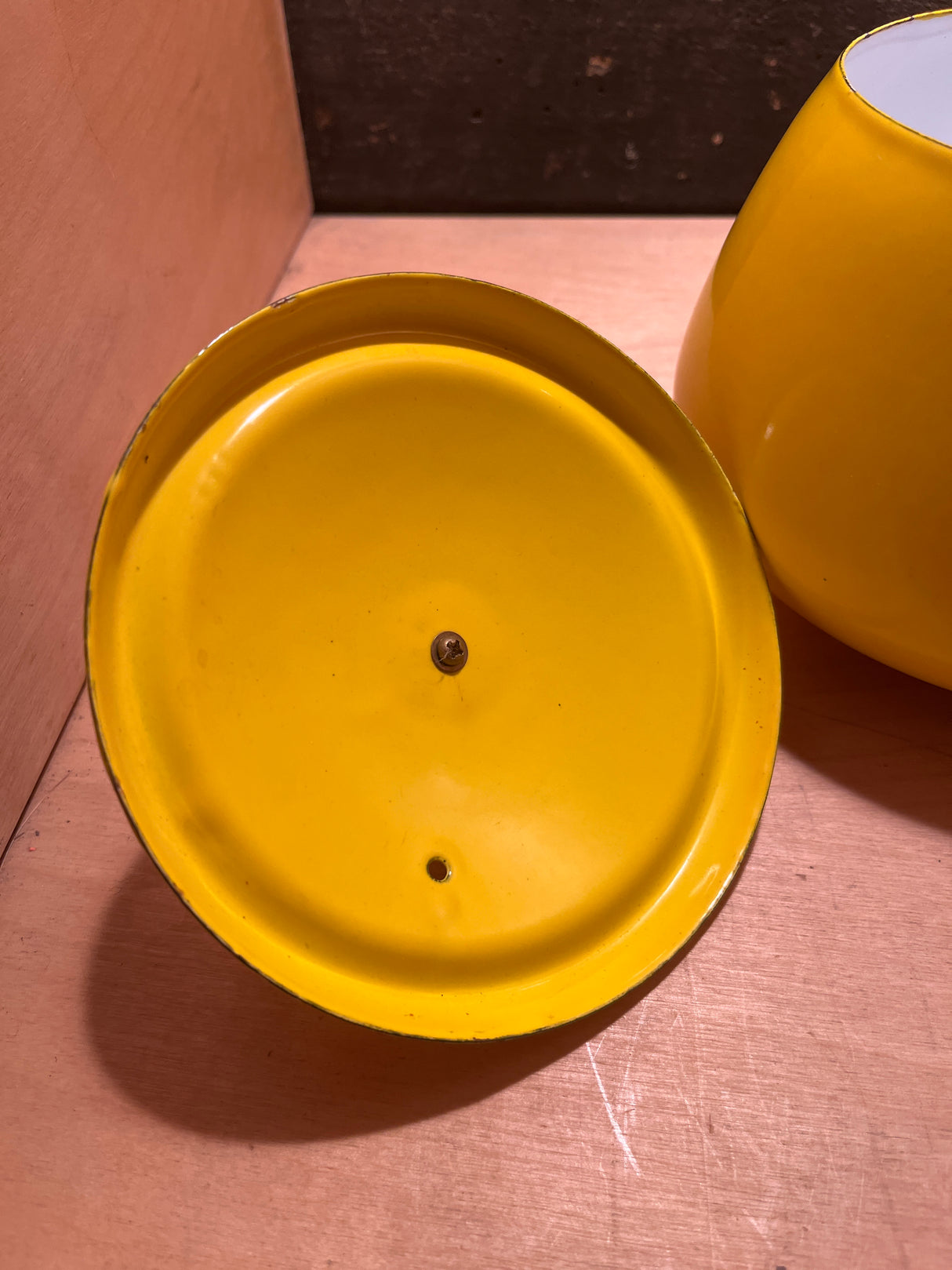 Vintage enamel sunshine yellow fondue pot with wood handles, featuring a circular dish-like base with a central screw and an off-center hole.