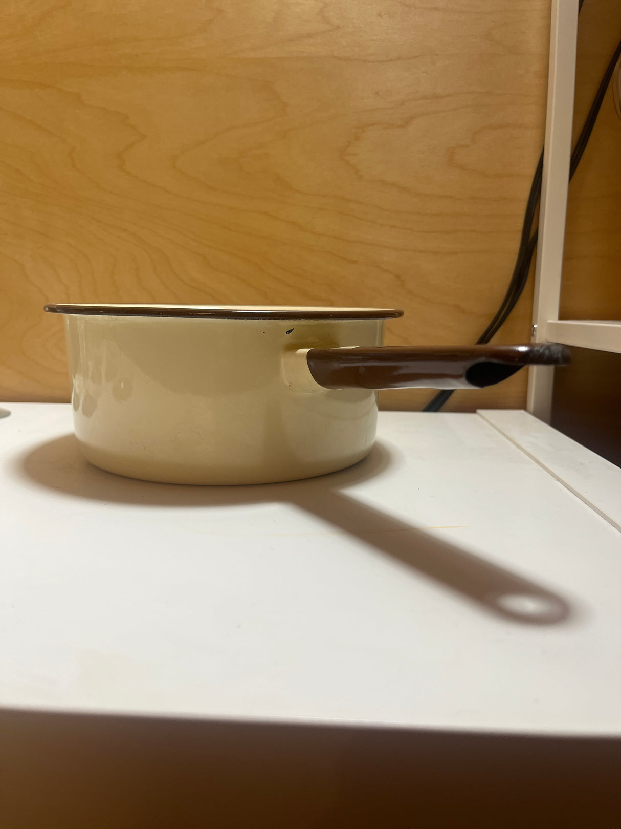 Tan and brown enameled sauce pot, featuring a chip on the handle end and a notch for hanging, adds a retro flair to your kitchen.