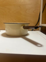 Tan and brown enameled sauce pot, featuring a chip on the handle end and a notch for hanging, adds a retro flair to your kitchen.