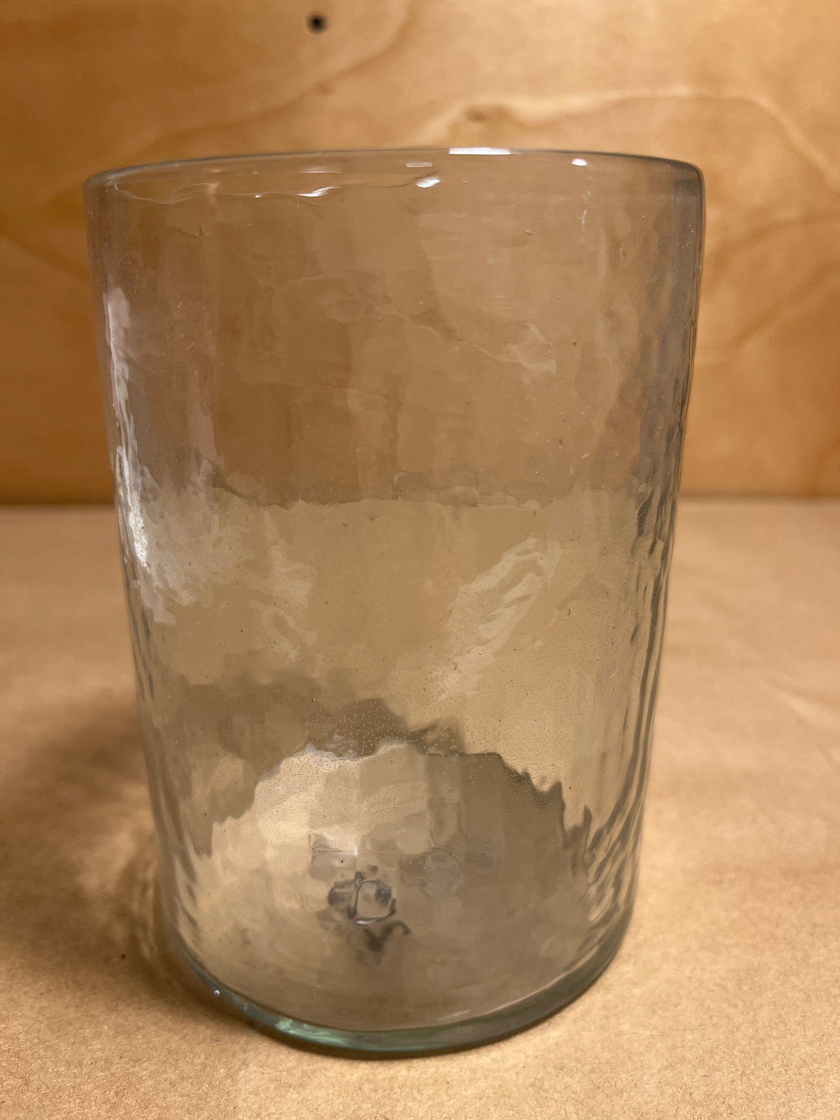 Hammered glass tumbler with a subtly dimpled texture and rounded rim, displayed upright, highlighting its clear, slightly hammered design.
