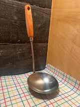 Stainless steel ladle with wood handle - EKCO Eterna, featuring a wide base and durable construction, resting on a patterned cloth.
