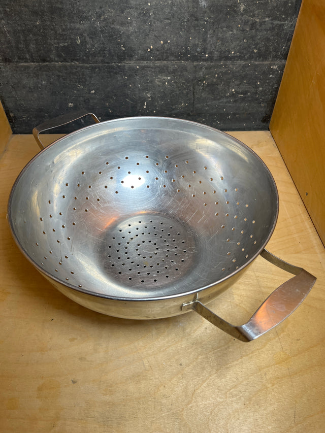 Large colander with handles and elevated base - stainless steel - Sharda, on a wooden surface, perfect for draining pasta and vegetables.