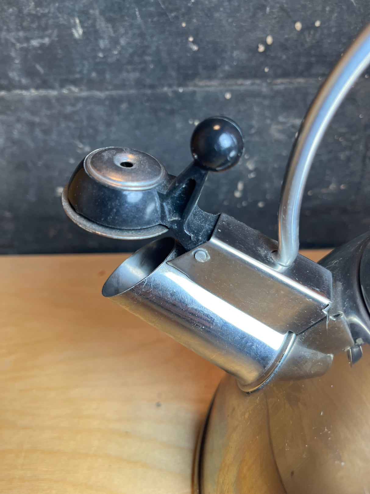 Whistling tea kettle - Farberware 2.5 quart features a stainless-steel spout with flip-up cap, black handle with red accents, on a wooden surface.